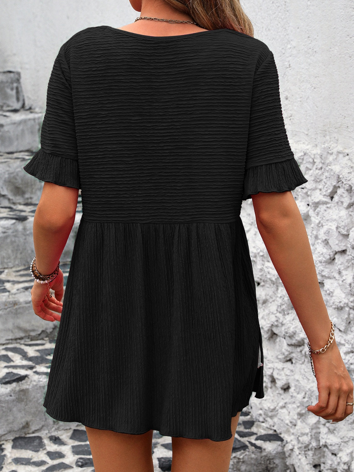Black textured babydoll blouse with flutter sleeves and smocked waist detail.