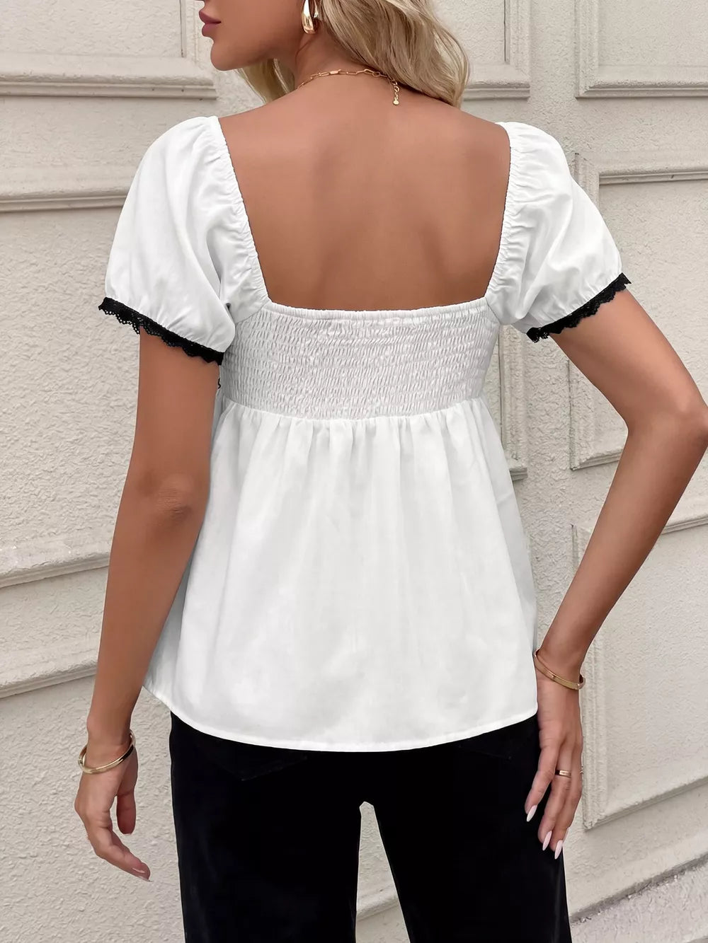 White short sleeve maternity blouse with smocked bodice and black lace trim on sleeves.