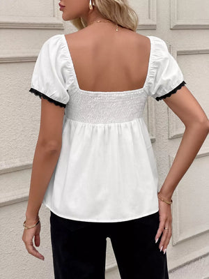 White short sleeve maternity blouse with smocked bodice and black lace trim on sleeves.