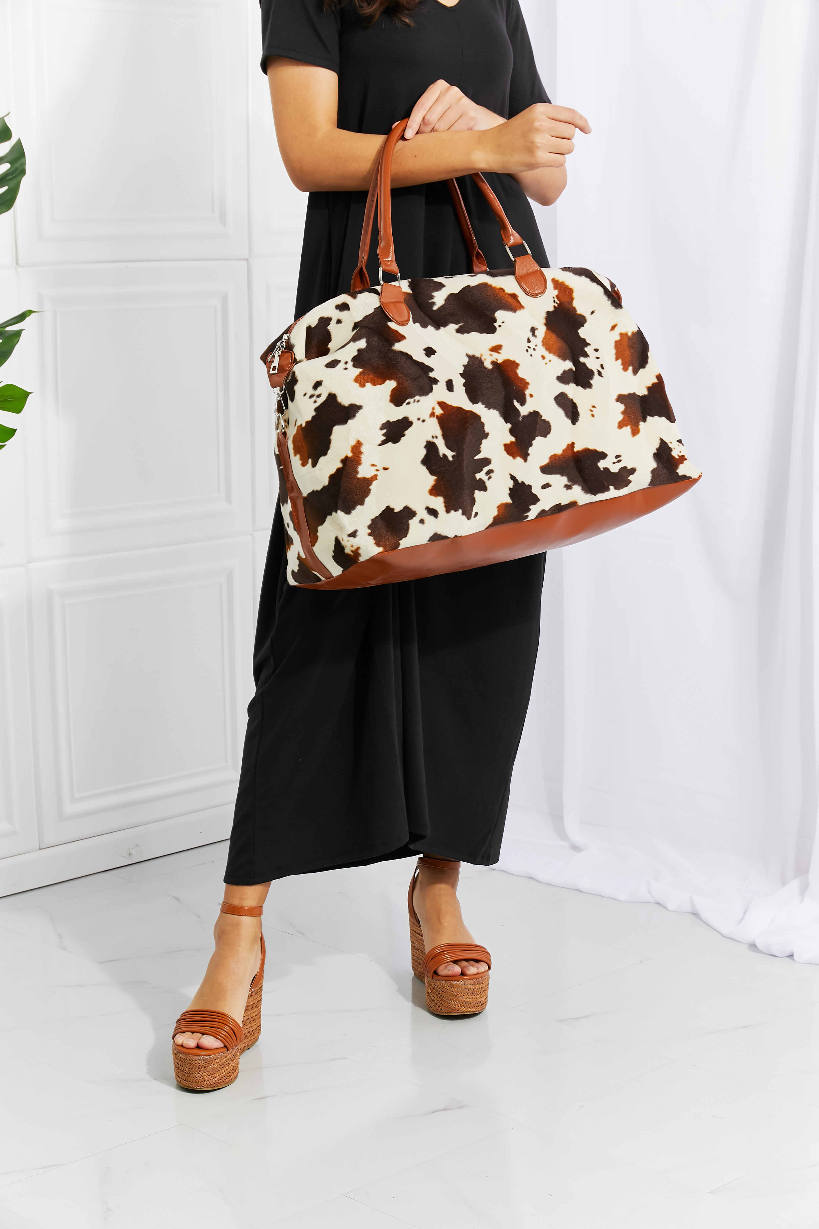Cowhide print duffel bag with brown leather trim and handles.