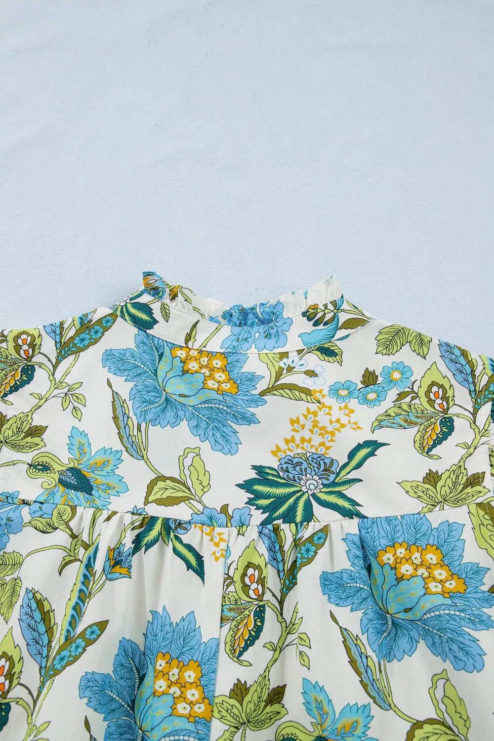 Floral mini dress with ruffled neckline and blue, green, yellow floral print on white cotton.