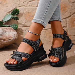 Black textured open-toe wedge sandals with adjustable straps and bow detail.