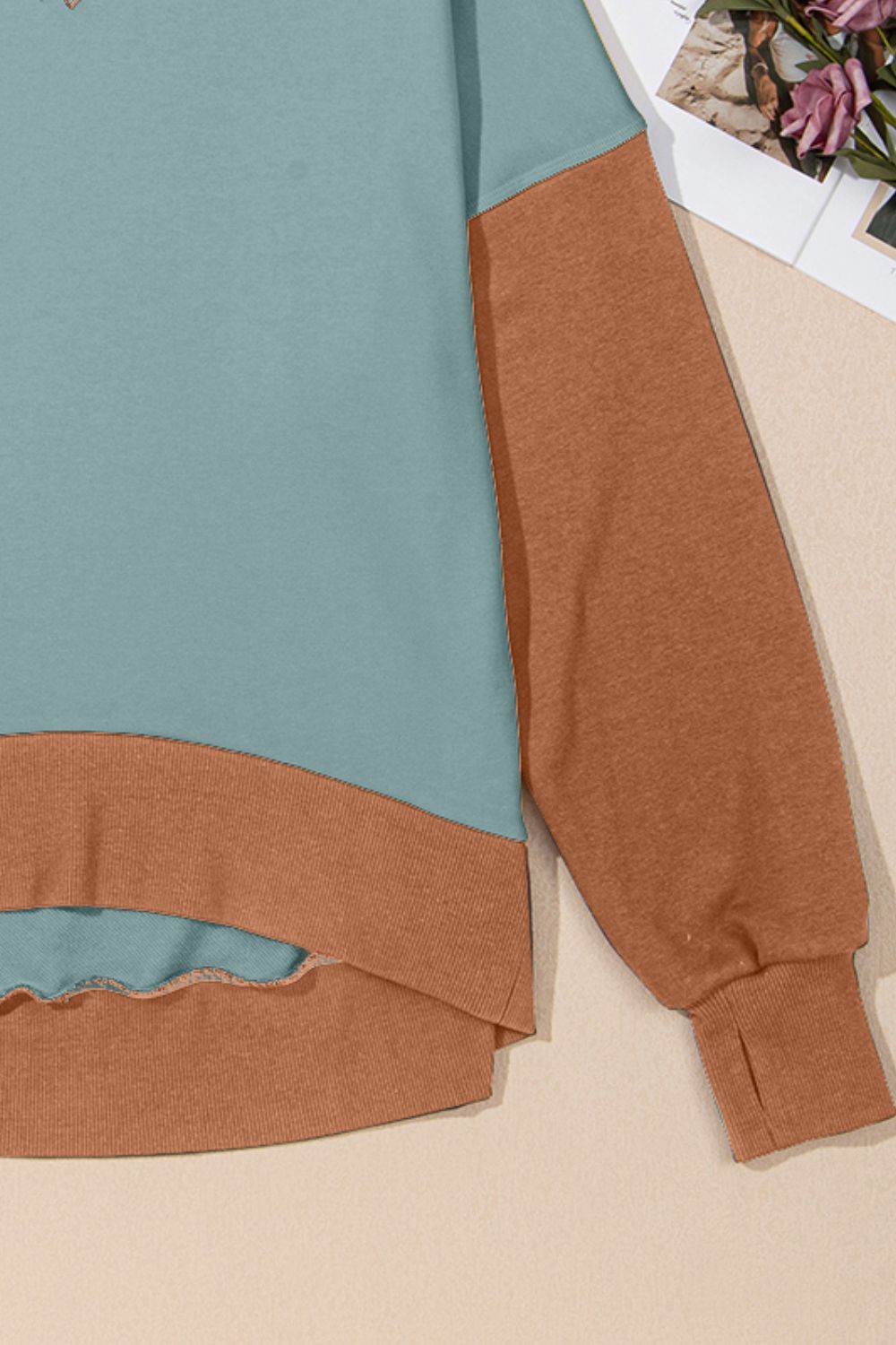 Crewneck sweatshirt with turquoise body and tan sleeves and hem detail.
