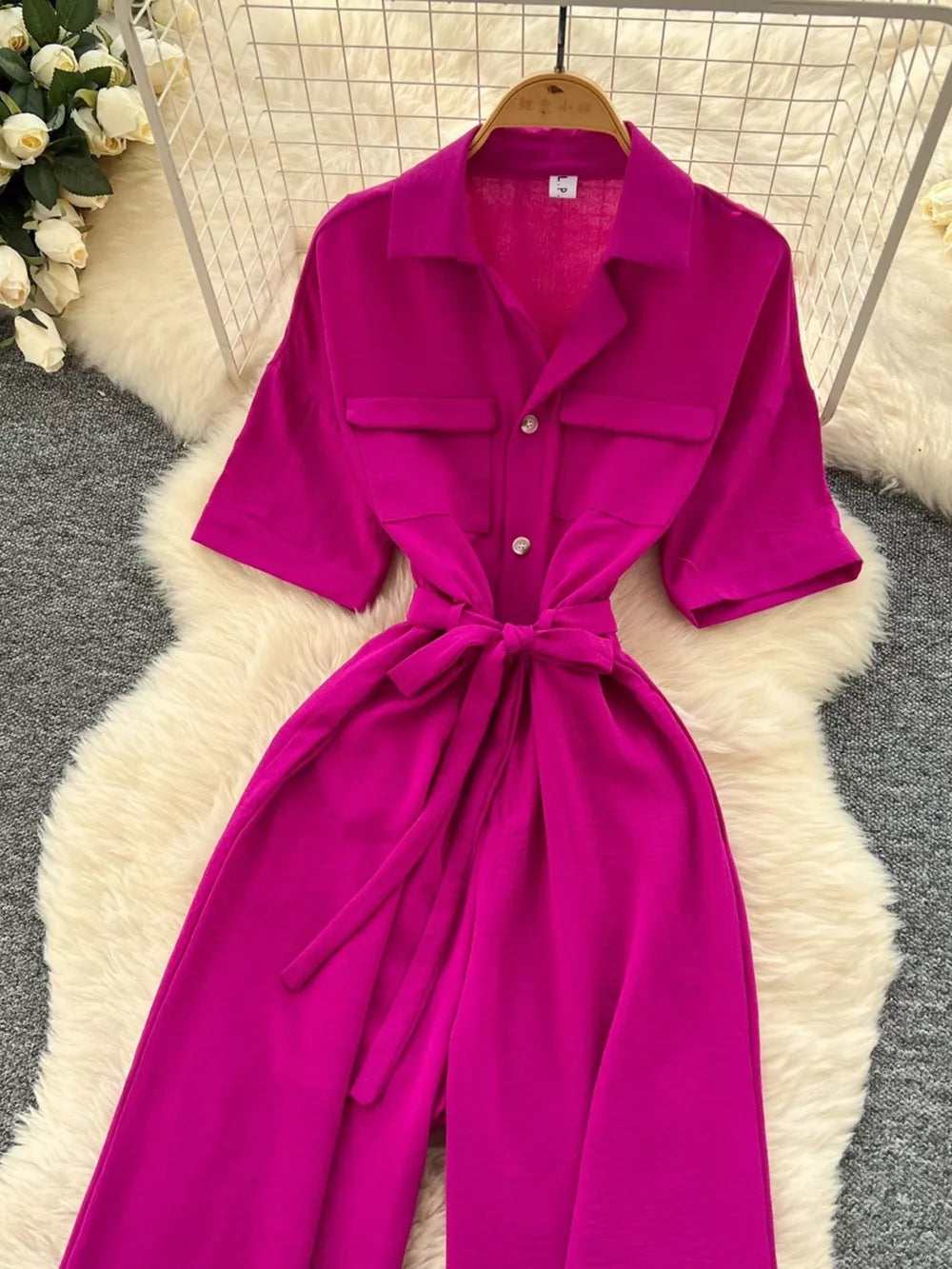 Belted wide-leg jumpsuit in pink with short sleeves, collar, button front, and tie waist.