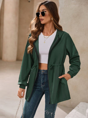 Dark green hooded jacket with cinched waistline and zip front, styled with jeans.