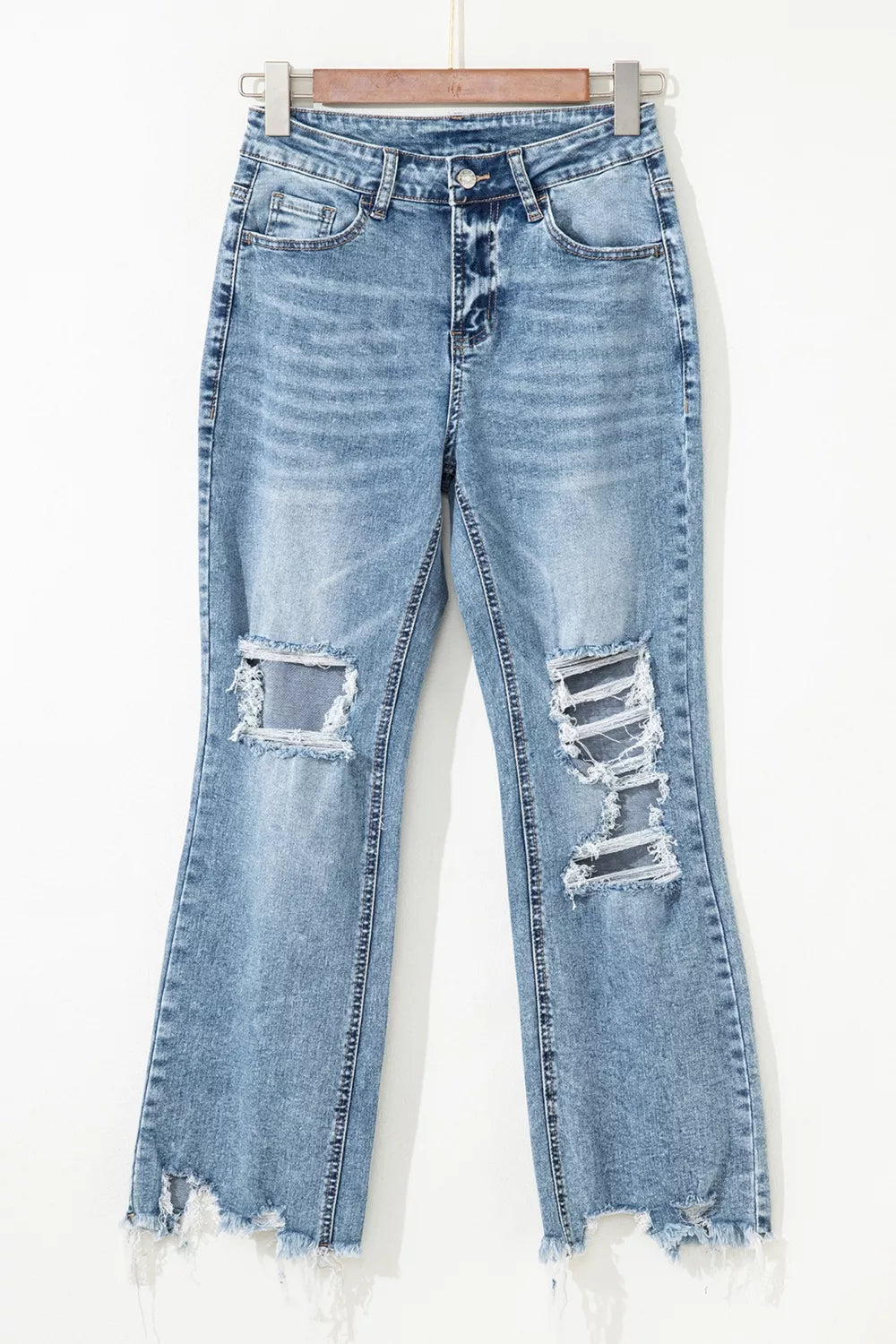 Distressed light wash denim flare jeans with open knees and raw hem.