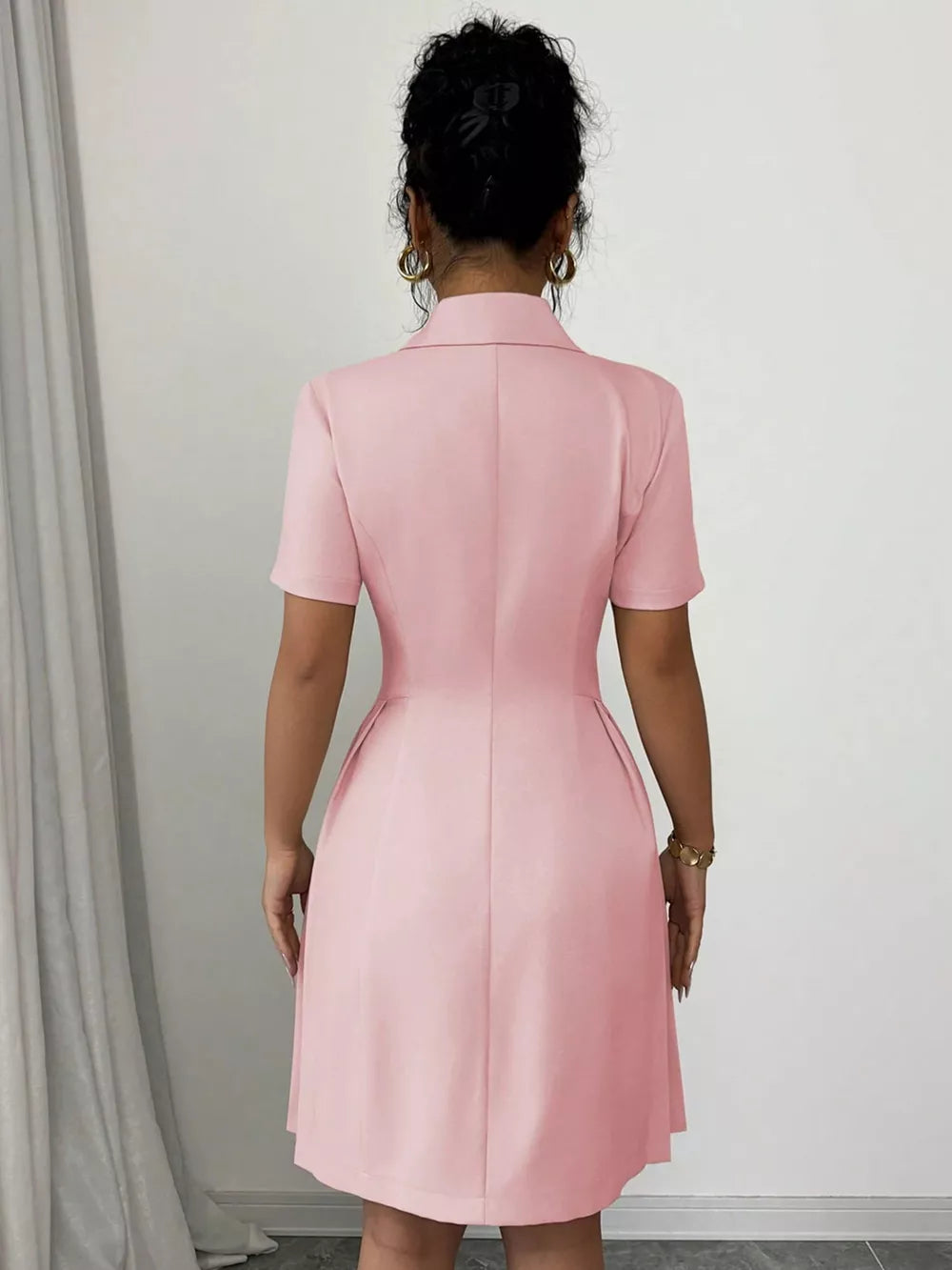 Blush pink double-breasted pleated blazer dress with short sleeves and a collared neckline.