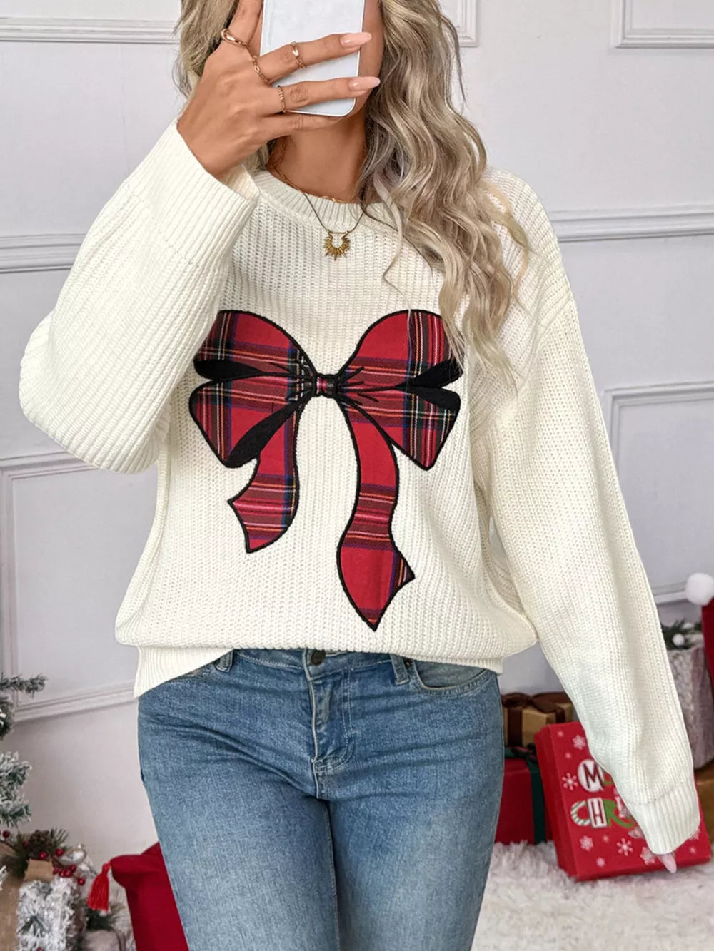 Cream ribbed knit sweater with a red plaid bow detail, crew neck, long sleeves.