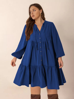 Plus-size dark blue tie-neck button-front tiered A-line dress with bell sleeves.