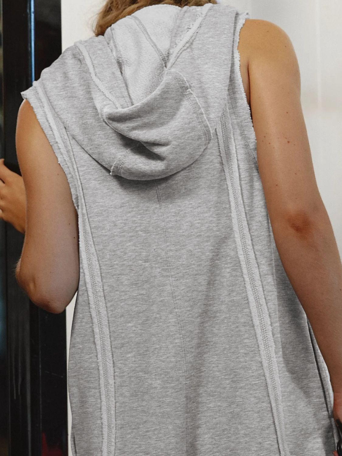 Gray sleeveless hooded romper with raw edges and contrast stitching detail.