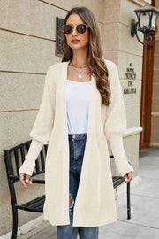 Cream knit cardigan with puffed sleeves and open front, styled with jeans.