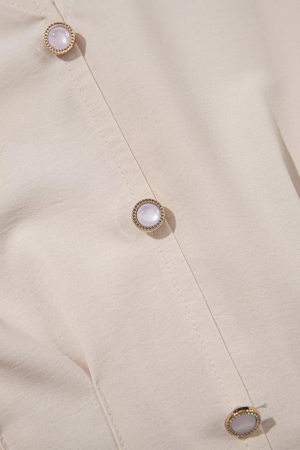 Elegant V-neck blouse in cream polyester with decorative pearl buttons and gold trim.