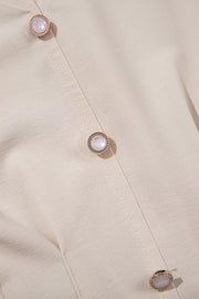 Elegant V-neck blouse in cream polyester with decorative pearl buttons and gold trim.