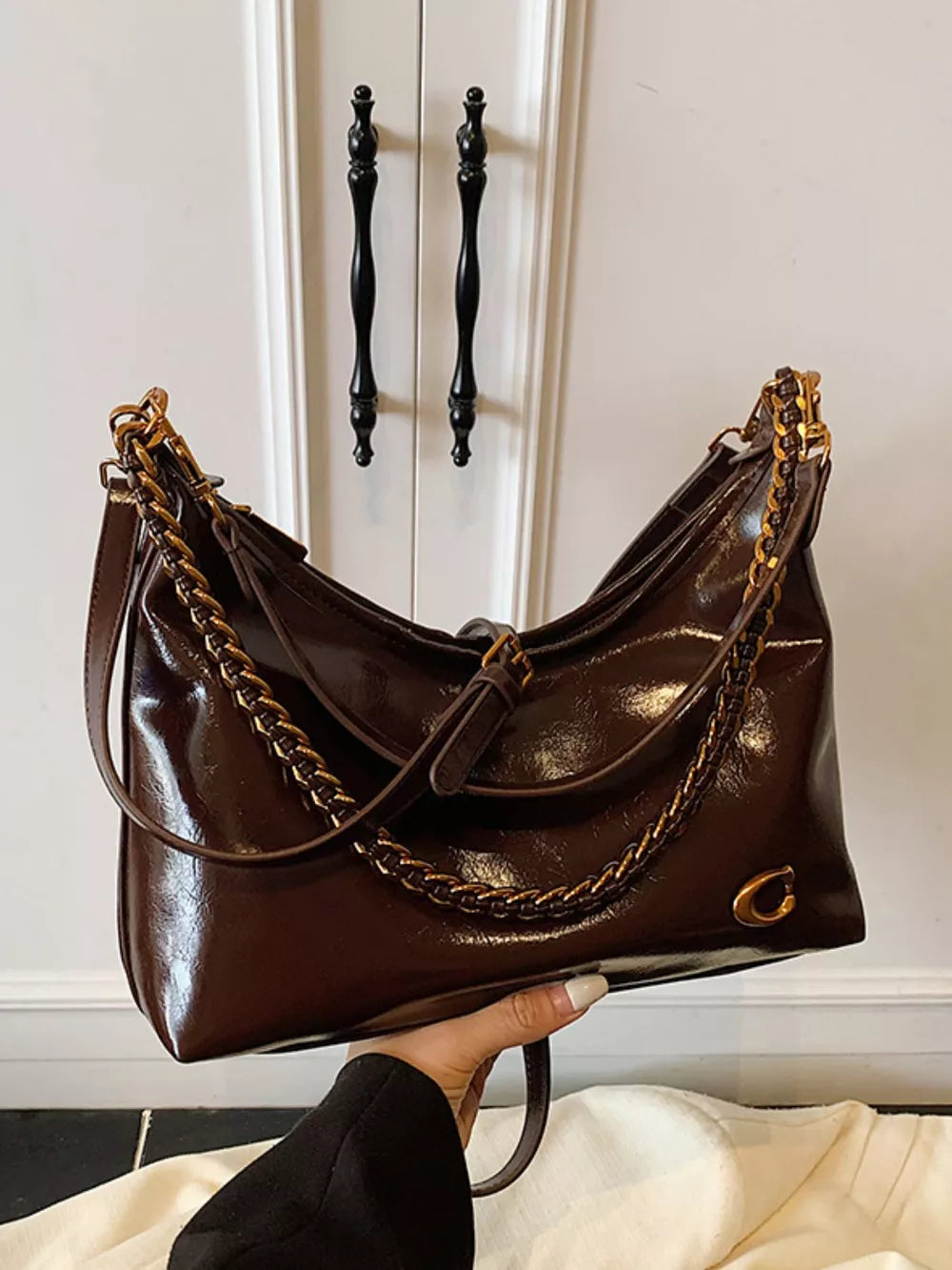 Brown patent leather crescent shoulder bag with gold chain detail and C logo