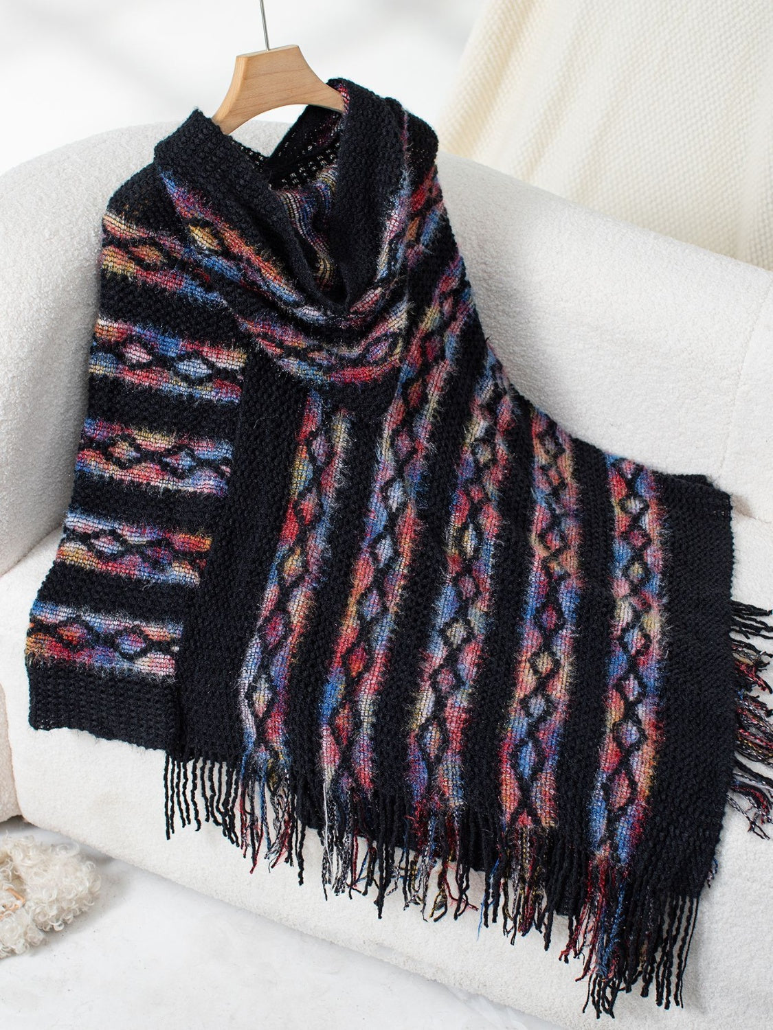 Black hooded knit cape with colorful diamond pattern and fringe detail