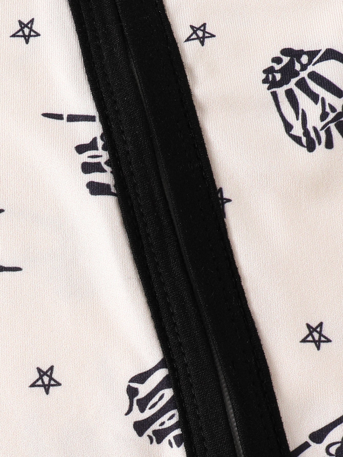 Beige baby one-piece with black skeleton hand and star print and black trim.