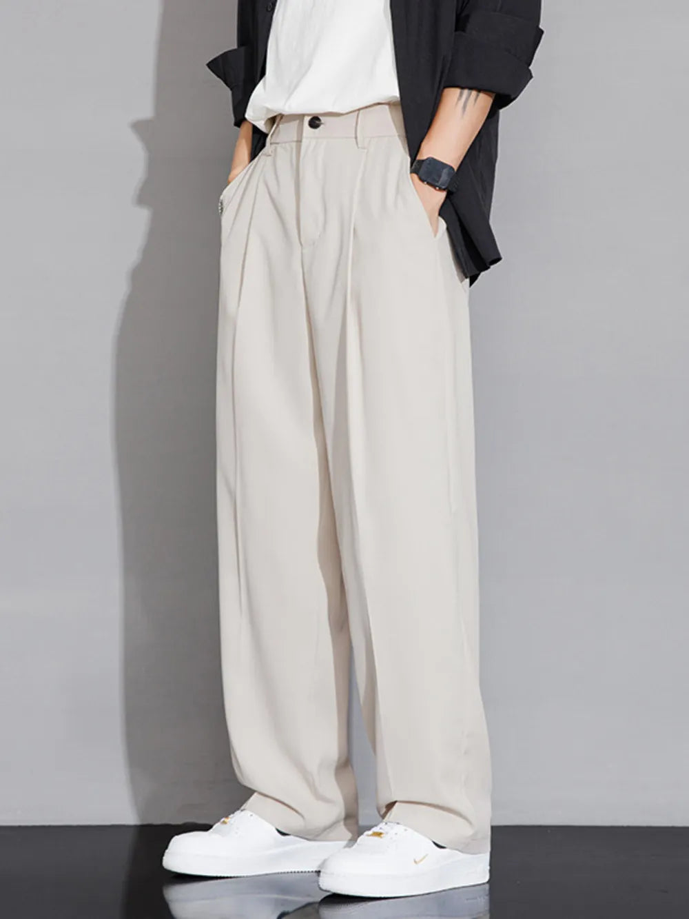 Men's beige wide-leg chinos with pleats and pockets, styled with a black jacket and white sneakers.