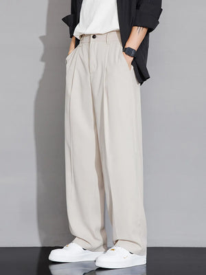 Men's beige wide-leg chinos with pleats and pockets, styled with a black jacket and white sneakers.