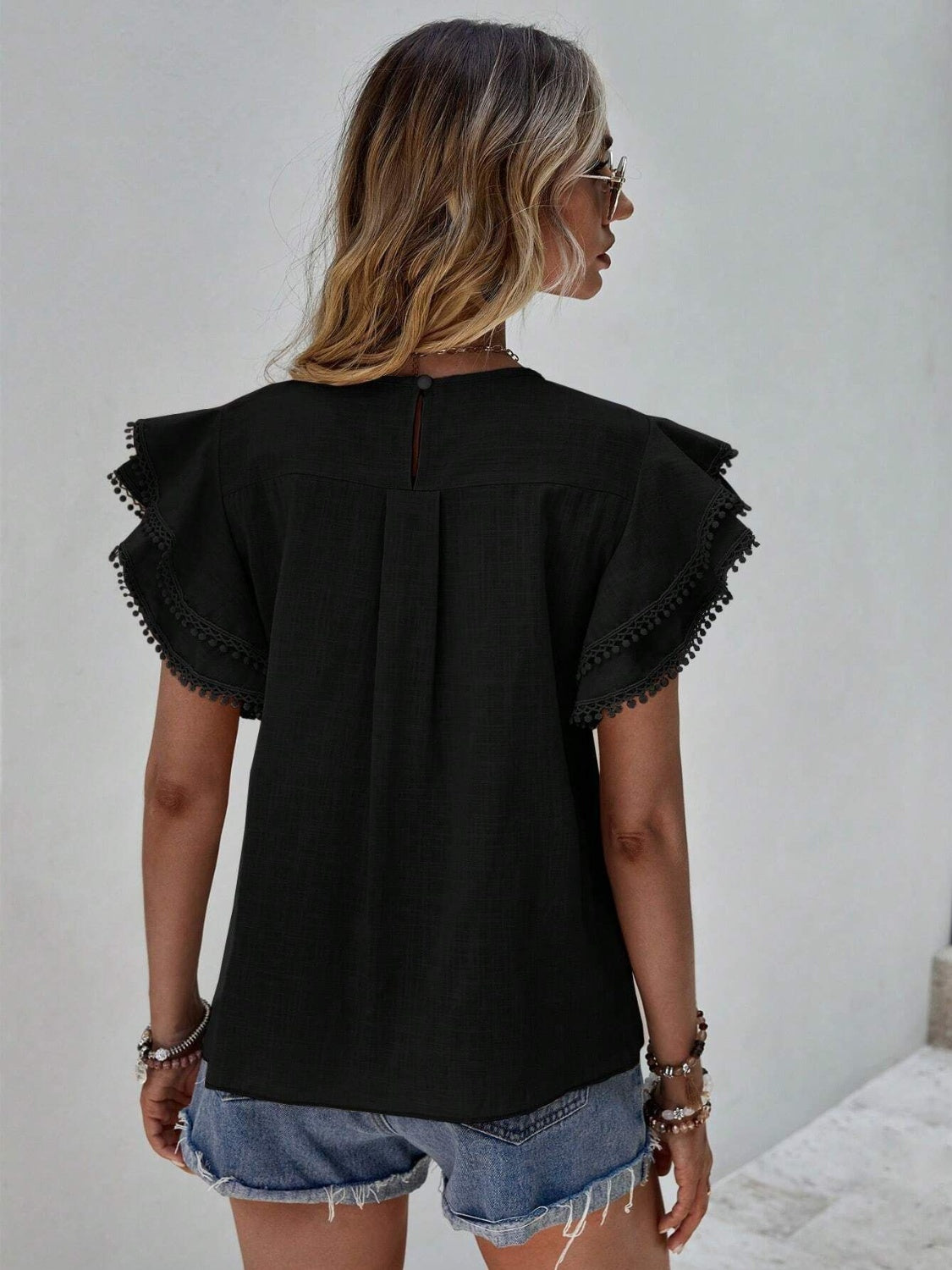 Black blouse with ruffle sleeves and pom-pom trim, back view.