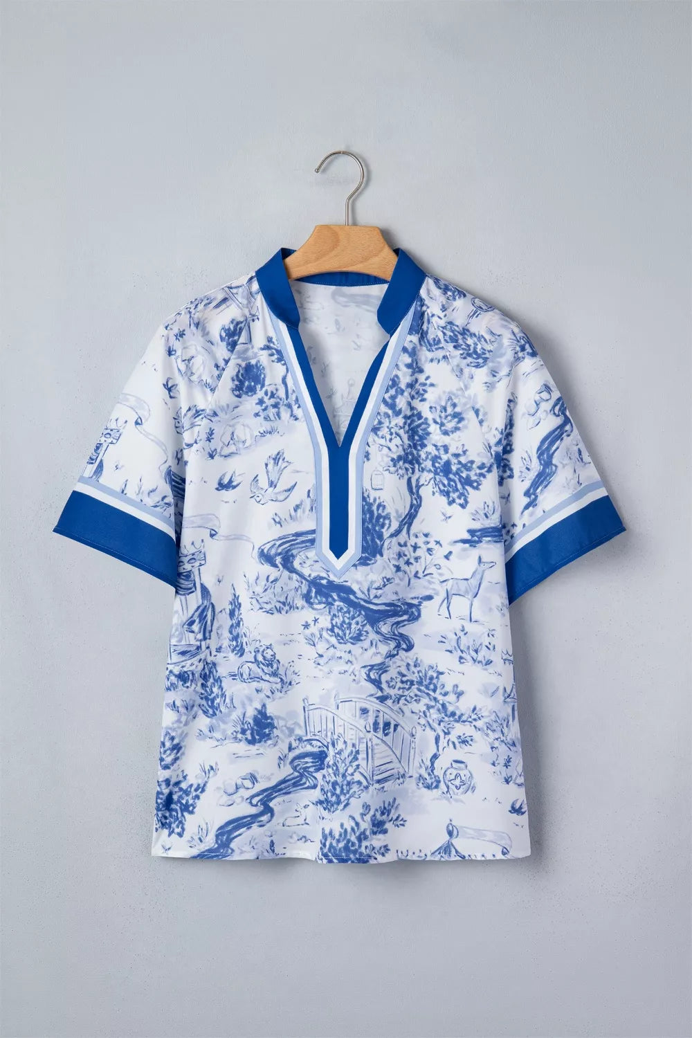 White polyester shirt with blue toile print, V-neck, short sleeves, and contrast trim.