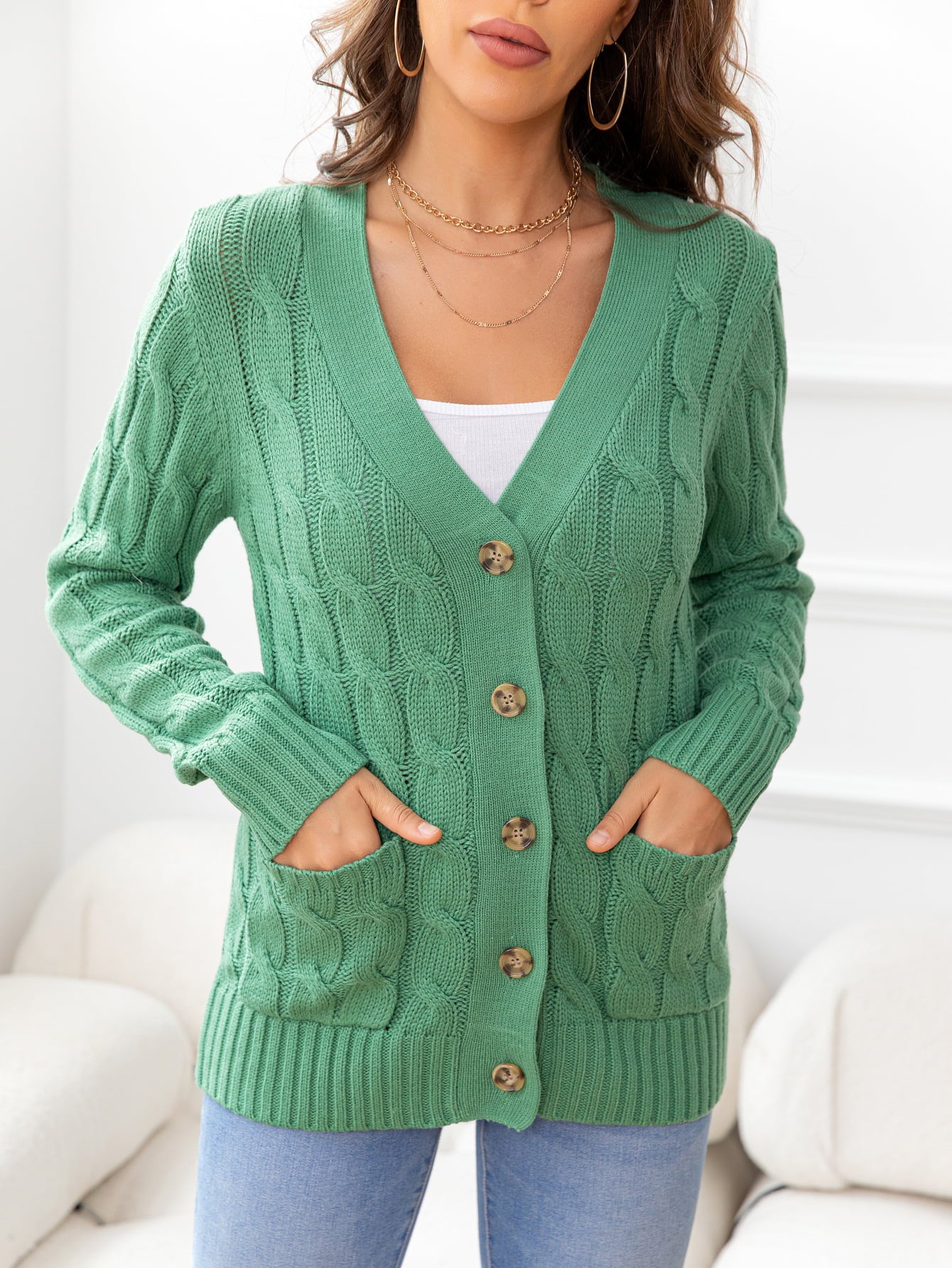 Green cable-knit cardigan with button front and patch pockets.