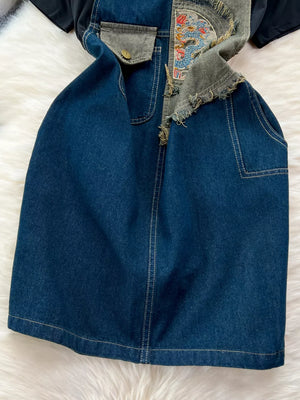 Denim overall dress with distressed details and embroidered patch, paired with a black knotted tee.