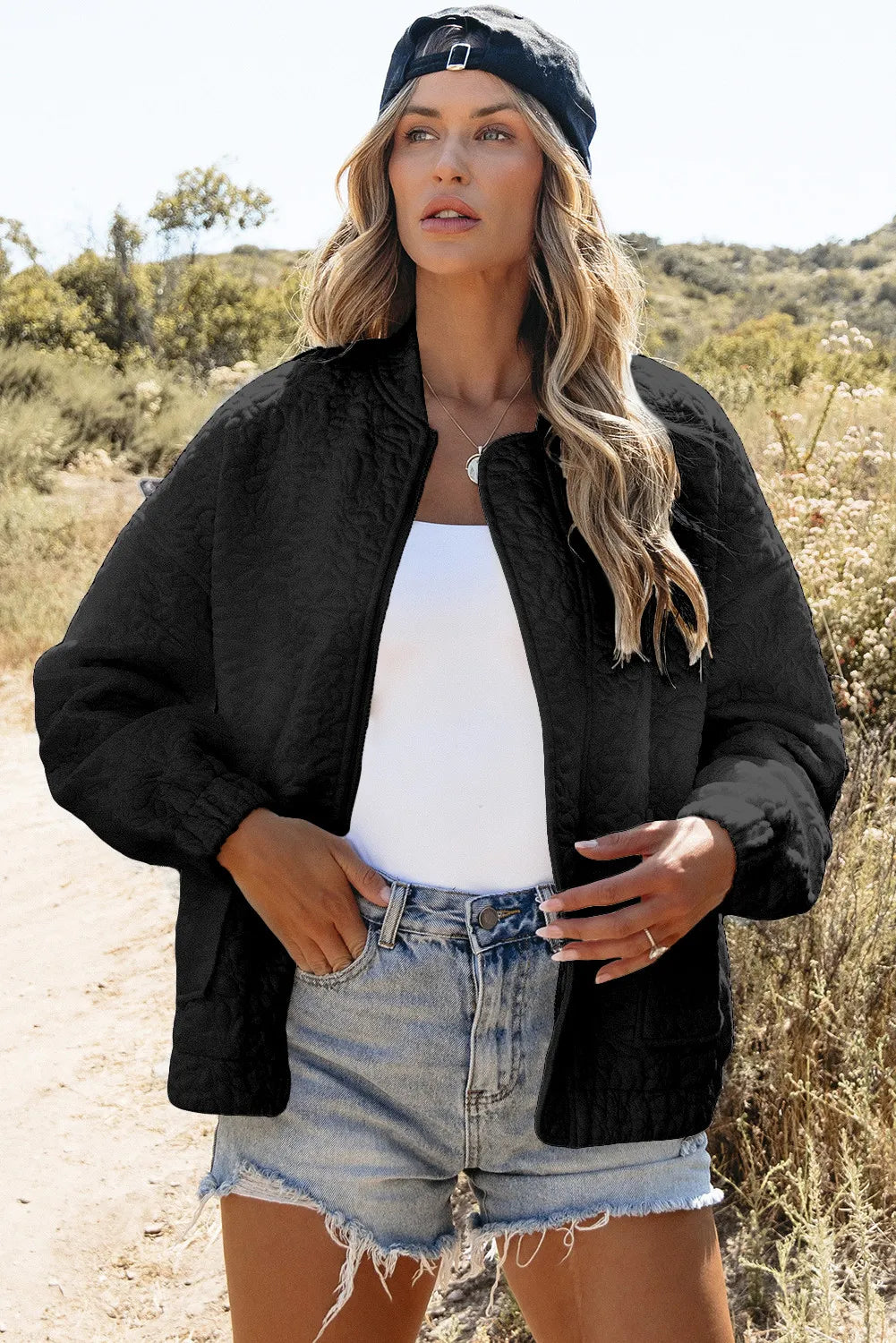 Black quilted bomber jacket with a round neckline and elastic cuffs, worn open over a white tank top.
