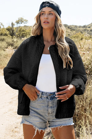 Black quilted bomber jacket with a round neckline and elastic cuffs, worn open over a white tank top.