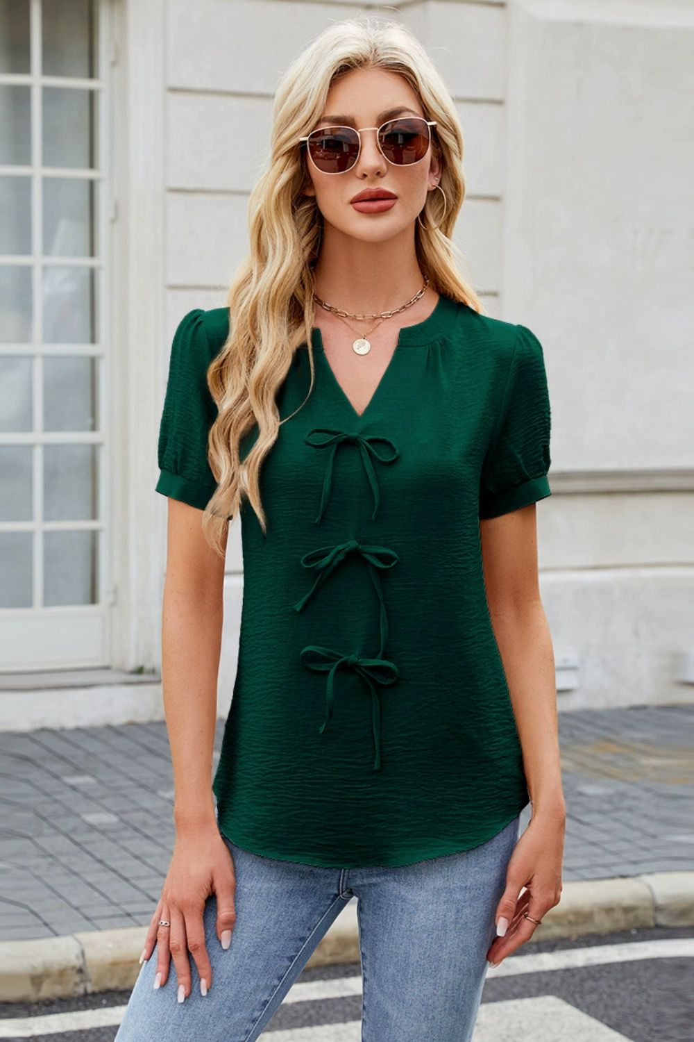 Dark green textured V-neck blouse with three bow details and short puff sleeves.