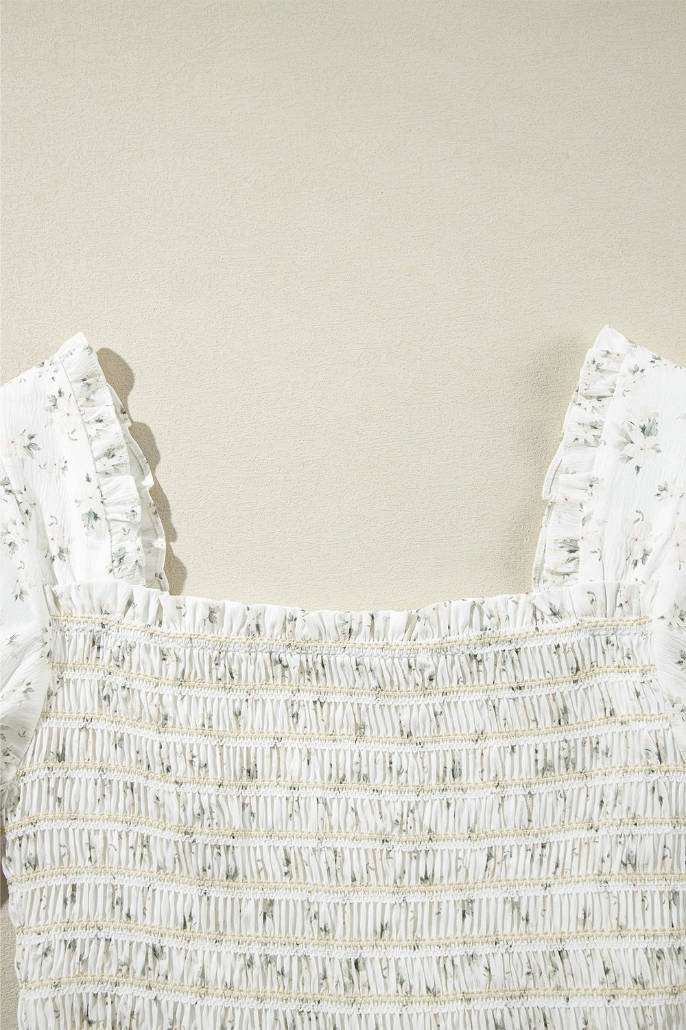White floral smocked bodice jumpsuit with ruffled square neckline and short sleeves.