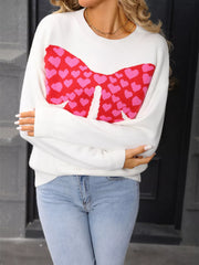 White knit sweater with red and pink heart bow graphic, round neck, long sleeves.