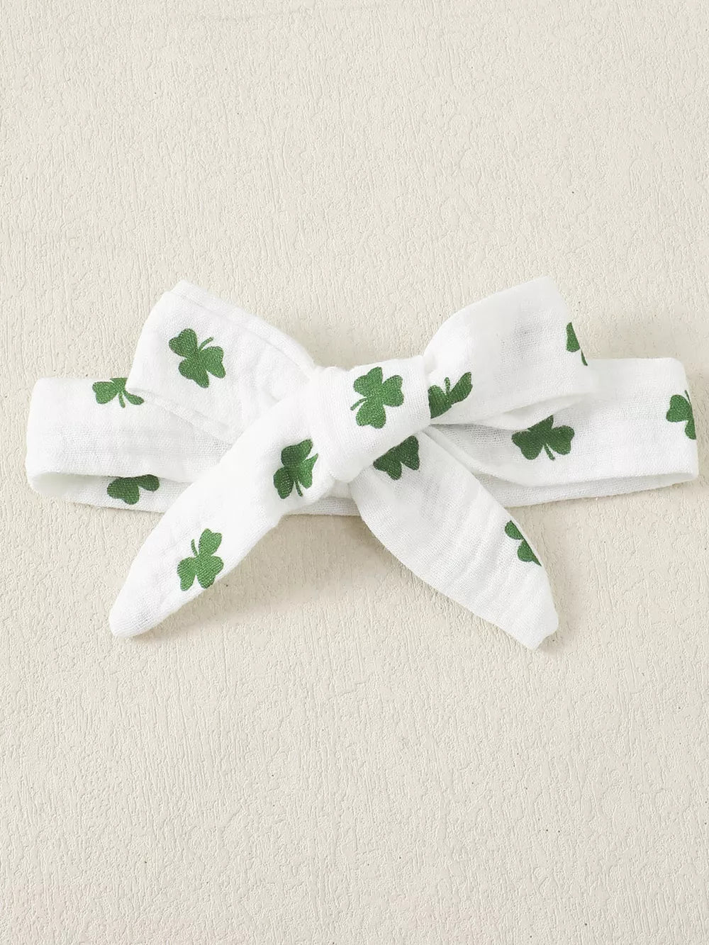 White cotton baby headband with green shamrock print and a bow detail.