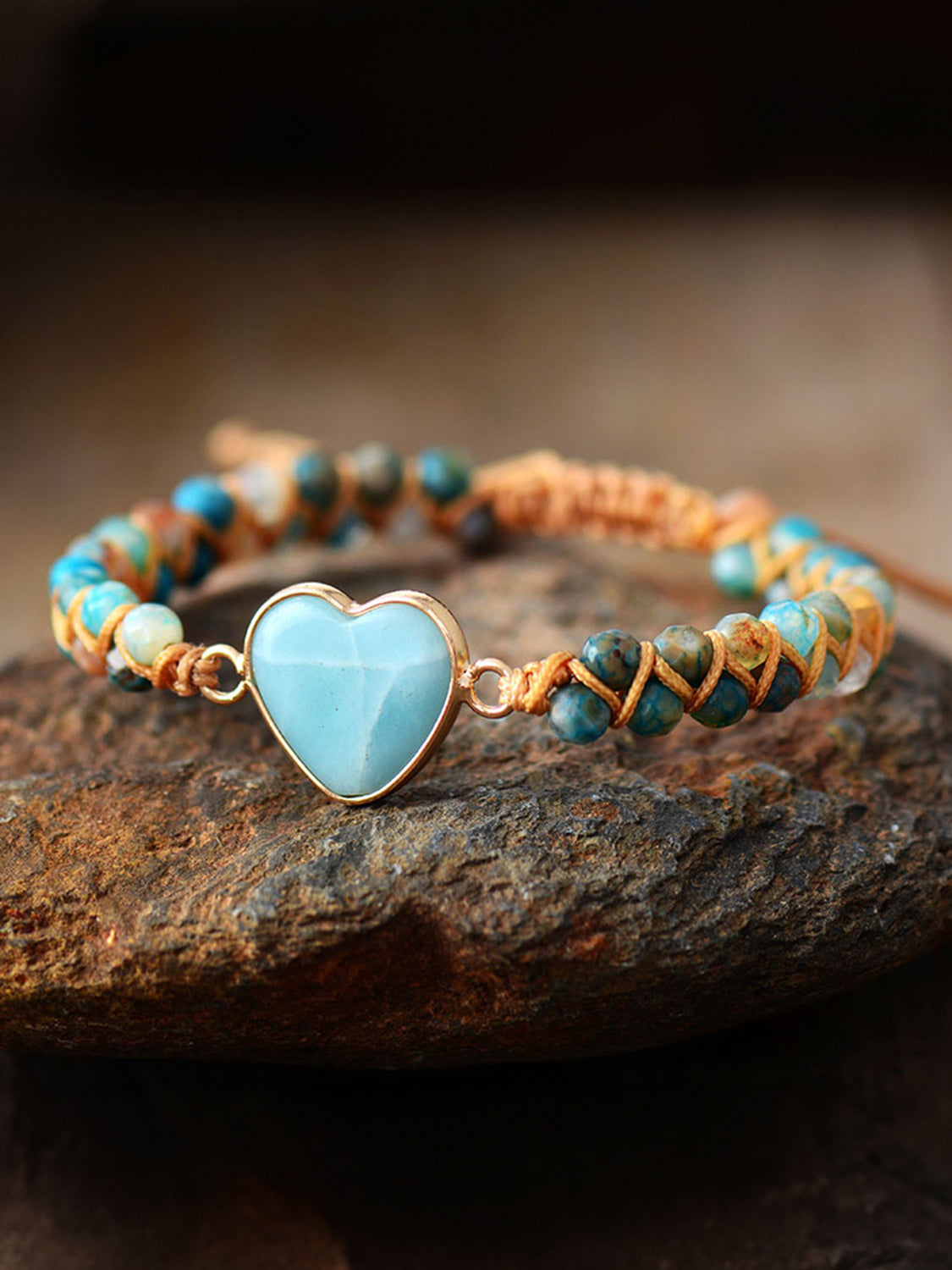 Light blue heart stone macrame bracelet with beaded accents on a stone surface.