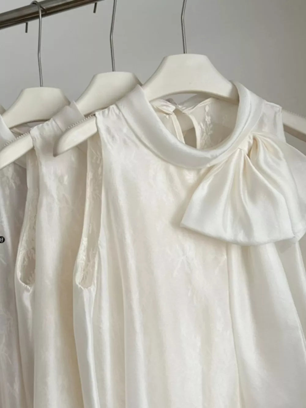 Sleeveless white shirt with a large bow detail at the neckline and subtle floral pattern.