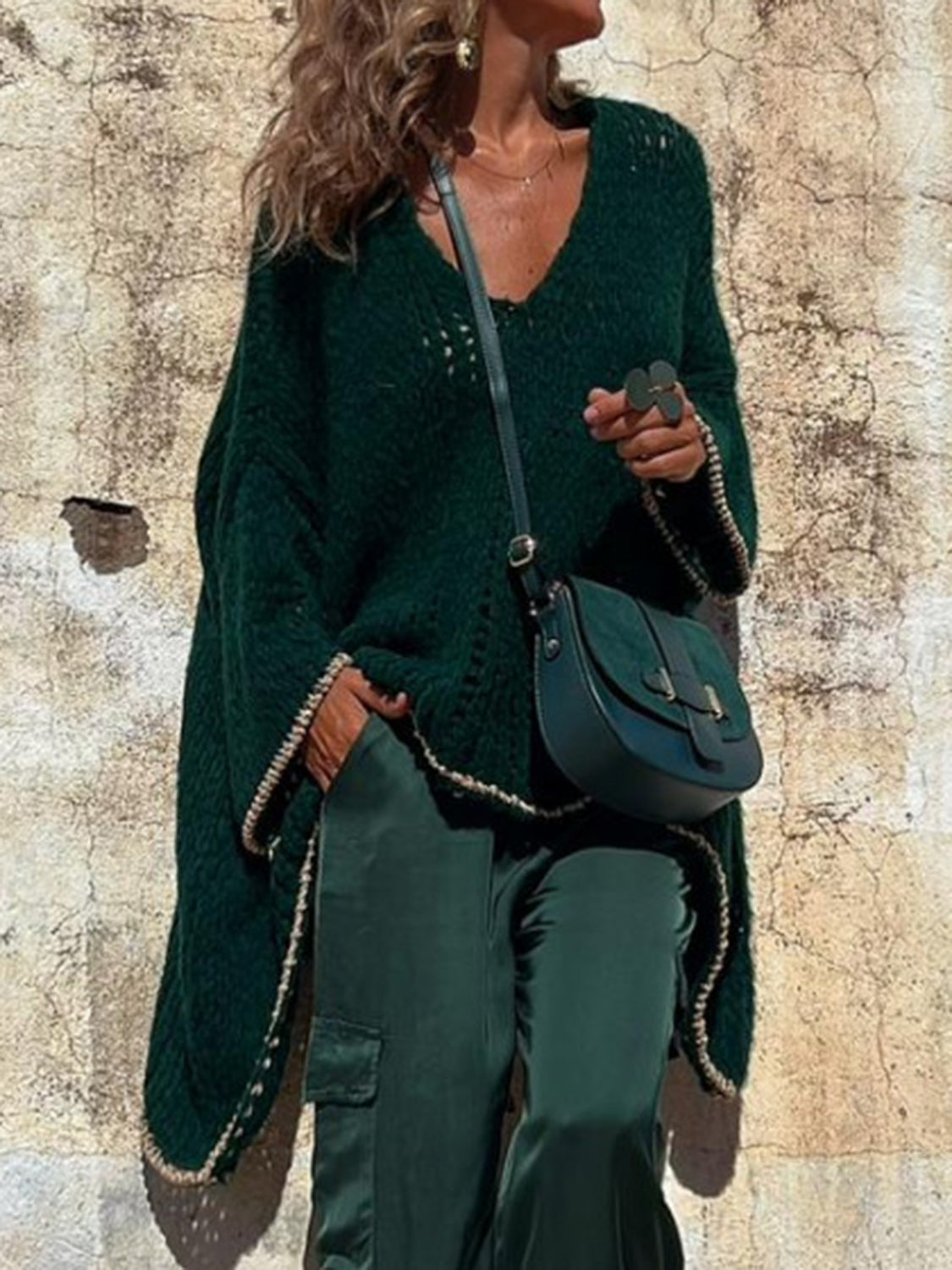 Dark green open knit sweater with asymmetric hem and beaded trim, styled with a crossbody bag.