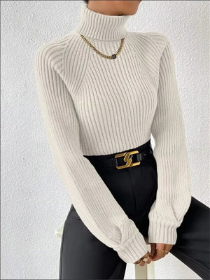 White ribbed turtleneck sweater with long sleeves and a high neck, styled with a gold chain necklace.