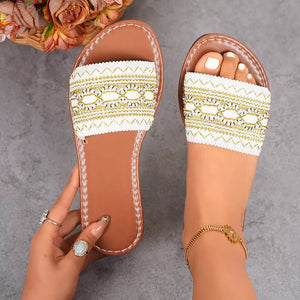 White embroidered artisan slide sandals with gold accents and a brown sole.