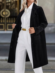 Black longline trench coat with lapel collar and buttoned front, worn open over white shirt and pants.