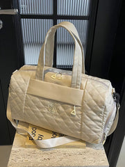 Diamond-stitched beige quilted duffel bag with adjustable strap and front logo detail.