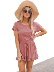 Blush pink romper with ruffle hem, drawstring waist, and short sleeves.