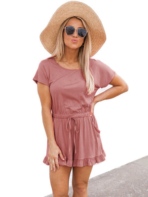 Blush pink romper with ruffle hem, drawstring waist, and short sleeves.