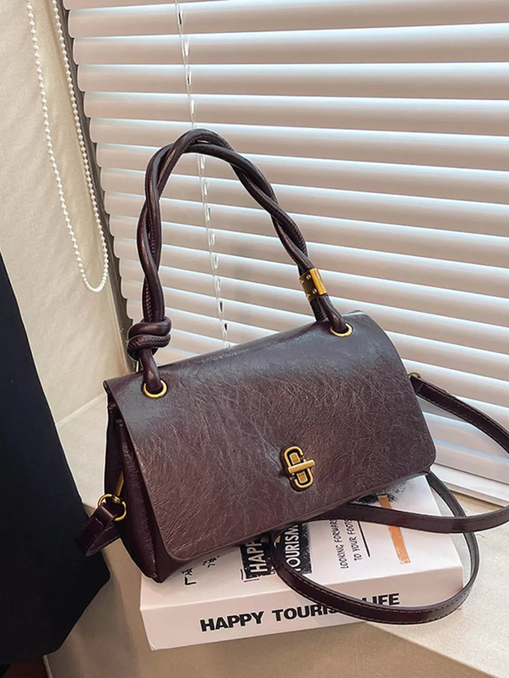 Chic brown crossbody bag with twisted handle and gold clasp detail.