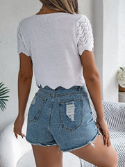 White crochet knit top with scalloped edge and eyelet sleeves, paired with distressed denim shorts.