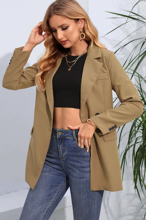 Tan double-breasted blazer with flap pockets and buttoned cuffs, worn over a black crop top and jeans.