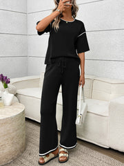 Black loungewear set with crew neck top and drawstring pants, detailed with white piping.