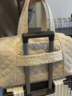 Diamond-stitched beige quilted duffel bag with embroidered name detail.