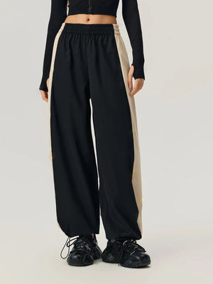 Black wide-leg track pants with beige side panels and drawstring hems.