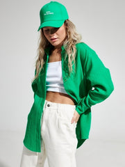 Green textured cotton overshirt with relaxed fit and button front, styled with white tank top and cream pants.
