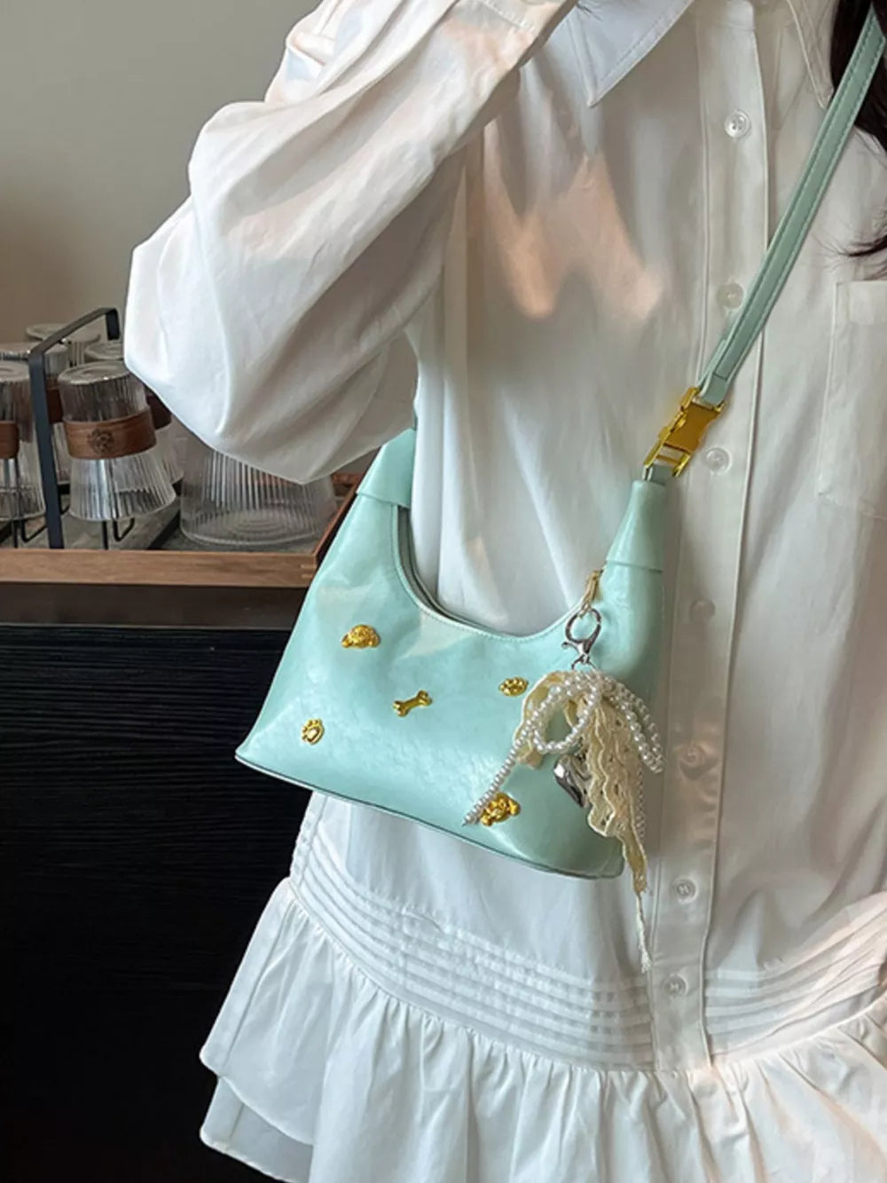 Pastel yellow hobo bag with gold accents and pearl charm, worn with a white dress.
