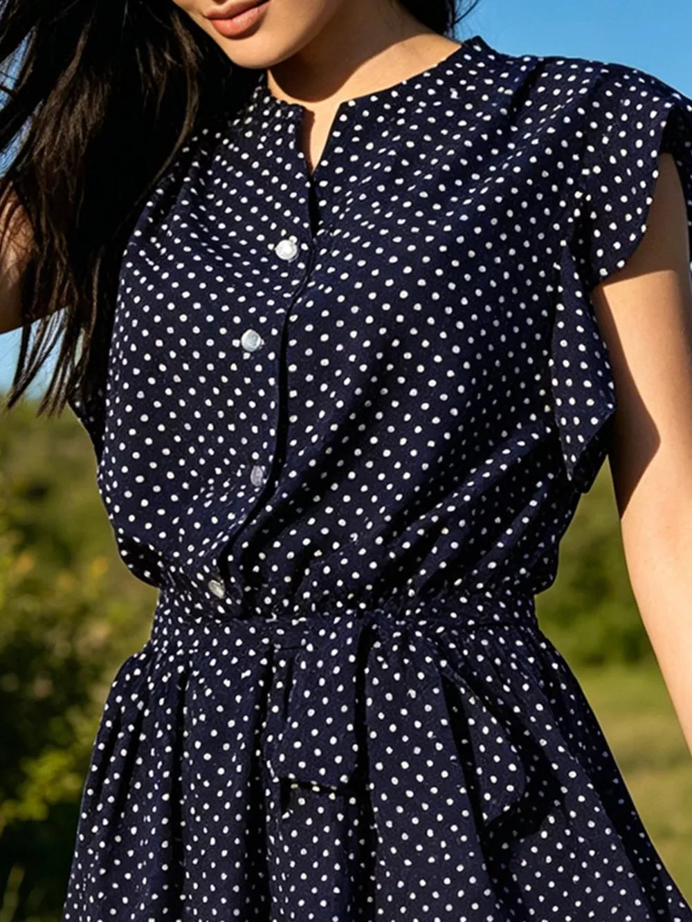 Navy polka dot dress with ruffle sleeves, button front, and tie waist detail.